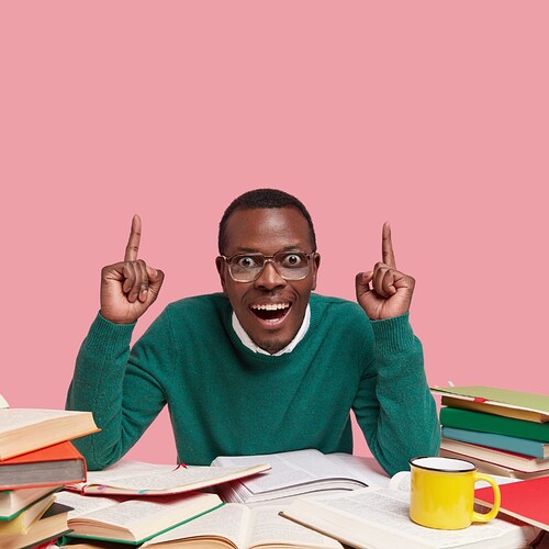 glad-astonished-black-male-green-jumper-points-with-both-index-fingers-has-toothy-smile-surrounded-with-many-books